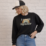 Person wearing a black sweatshirt with 'I could be meaner' text and rainbow design, standing against a brick wall.