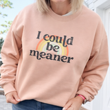 Woman wearing a pink sweatshirt with 'I could be meaner' text and rainbow design outdoors.