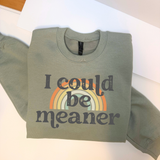Folded sage green sweatshirt with 'I could be meaner' text and rainbow design on a white surface.