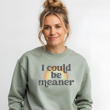 Woman wearing a sage green sweatshirt with 'I could be meaner' text and rainbow design.