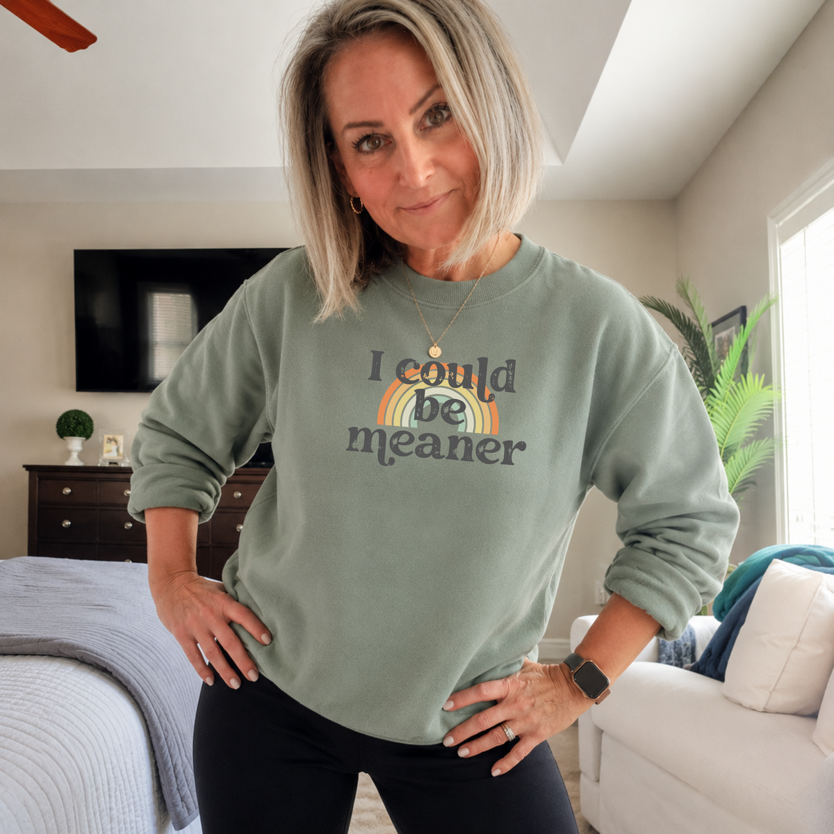 Woman wearing a green sweatshirt with 'i could be meaner' text  over a rainbow in a living room