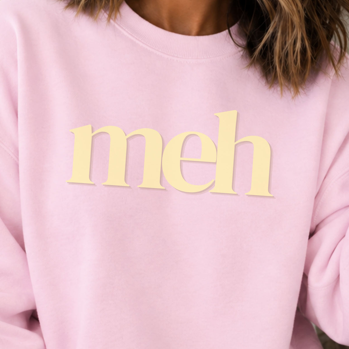 Close up of a pink sweatshirt with the word "meh" in yellow lettering.