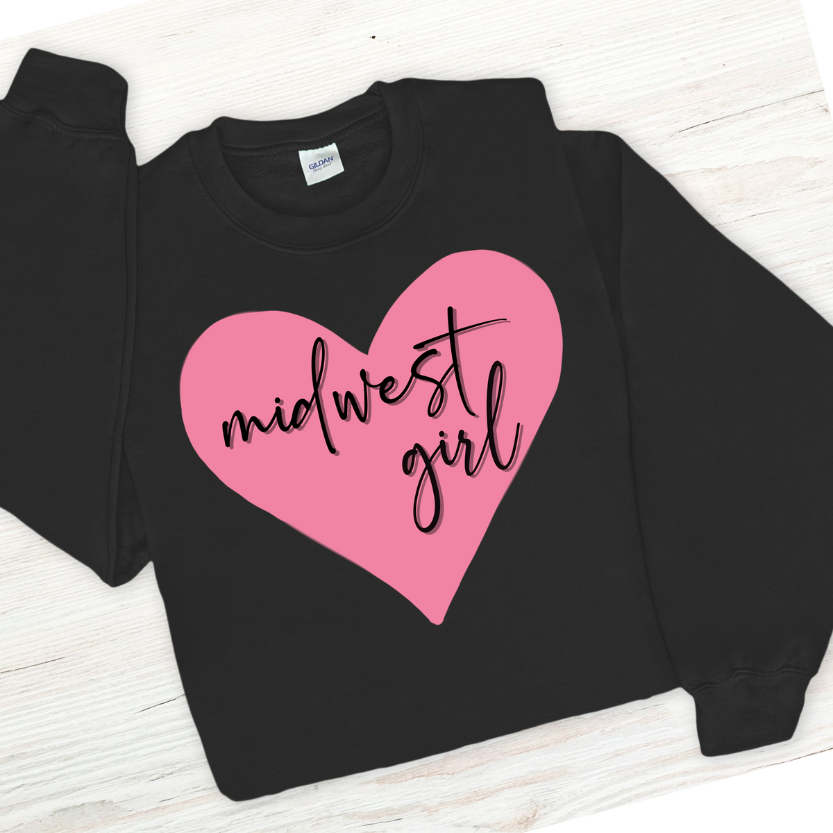 Black sweatshirt with a pink heart and 'midwest girl' text on a light wooden surface