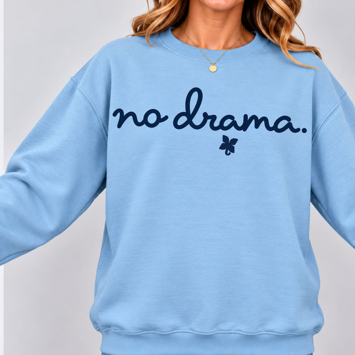 A person wearing a light blue crewneck sweatshirt with the text 'no drama.' in dark navy script and a small butterfly graphic underneath, shown against a light gray background.