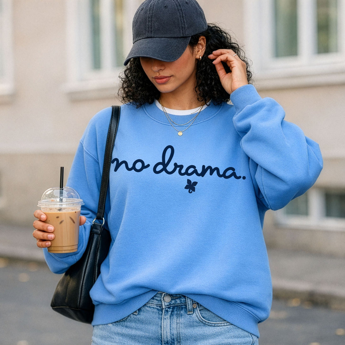 A woman in a light blue sweatshirt that says "no drama" holding an iced coffee.