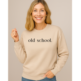 Woman wearing a beige sweatshirt with 'old school.' text on a plain background