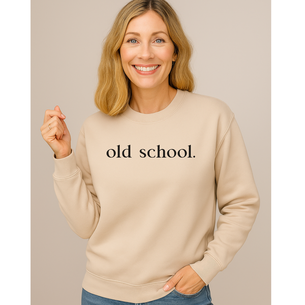 Woman wearing a beige sweatshirt with 'old school.' text on a plain background