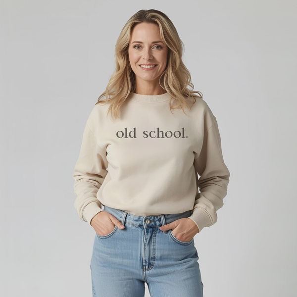 Woman wearing a beige sweatshirt with 'old school.' black text on a plain background