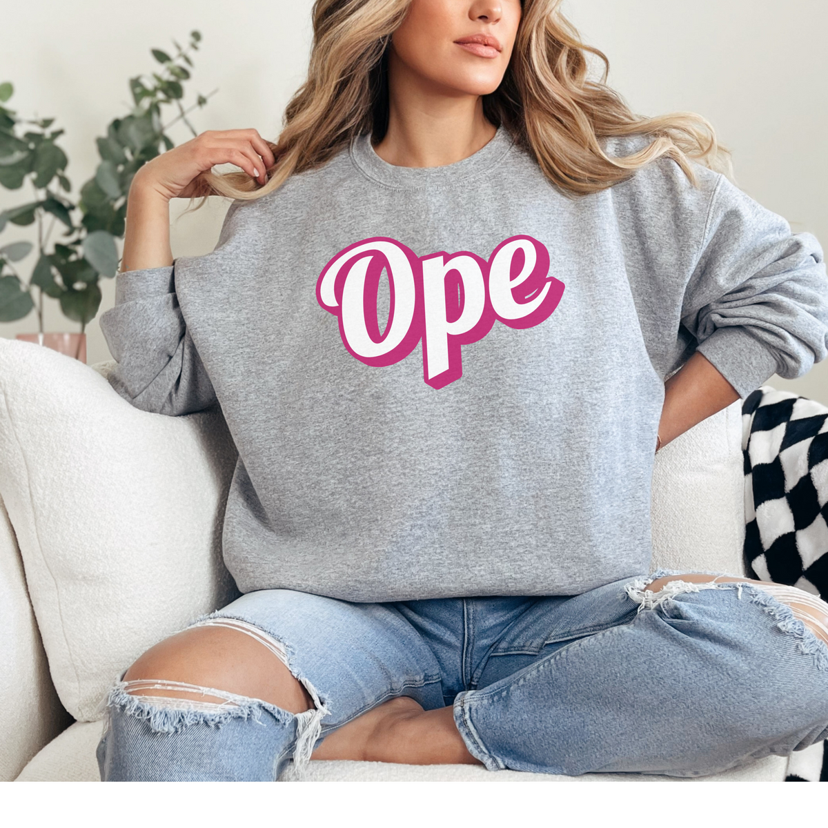 Person wearing a gray sweatshirt with 'Ope' in pink text, sitting on a couch.