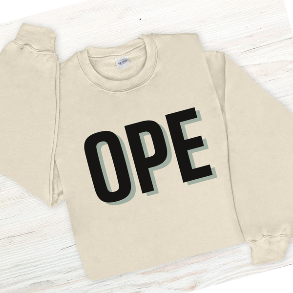 Beige sweatshirt with 'OPE' printed on it laid flat on a wooden surface