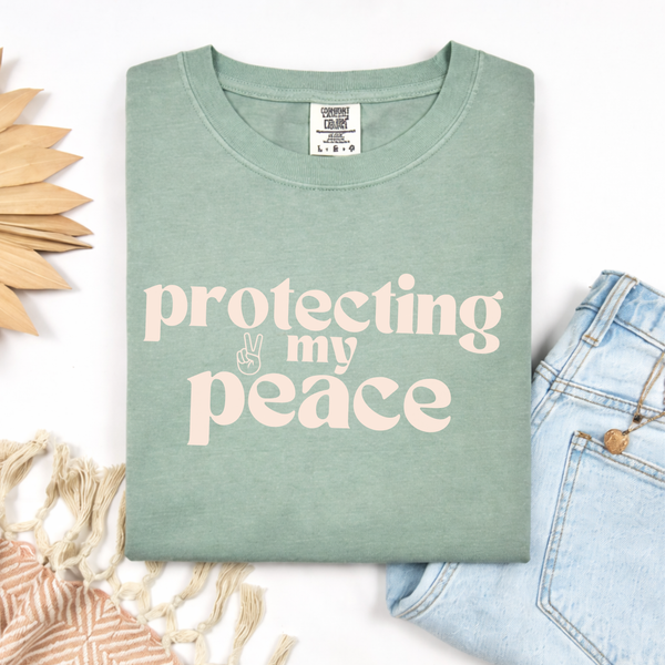 Folded green t-shirt with 'protecting my peace' text on a white background