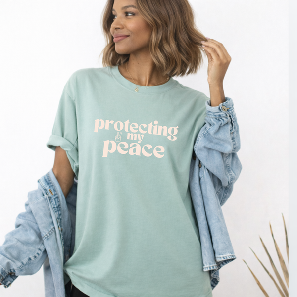 Woman wearing a light green t-shirt with 'protecting my peace' text, holding a denim jacket.