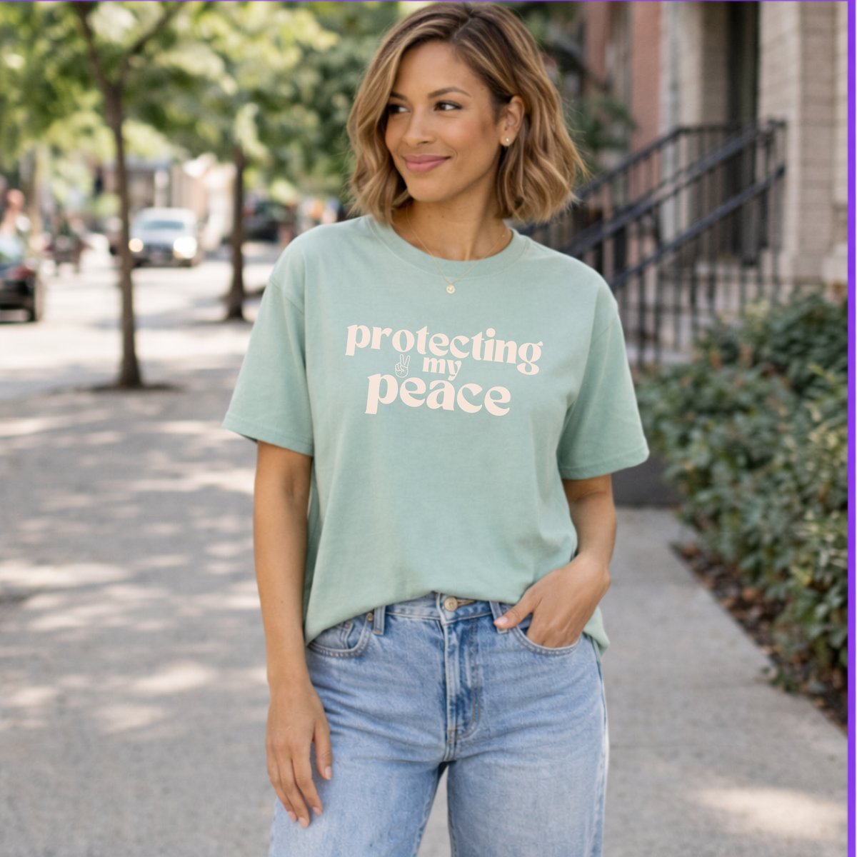 Woman wearing a light green t-shirt with 'protecting my peace' text, standing on a sidewalk.