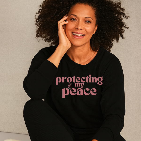 Woman wearing a black sweatshirt with 'protecting my peace' text, sitting against a neutral background.