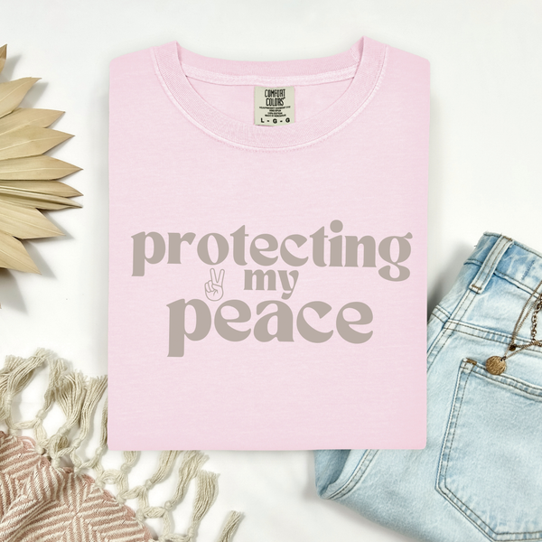 Pink t-shirt with 'protecting my peace' text on a white background with decorative elements.