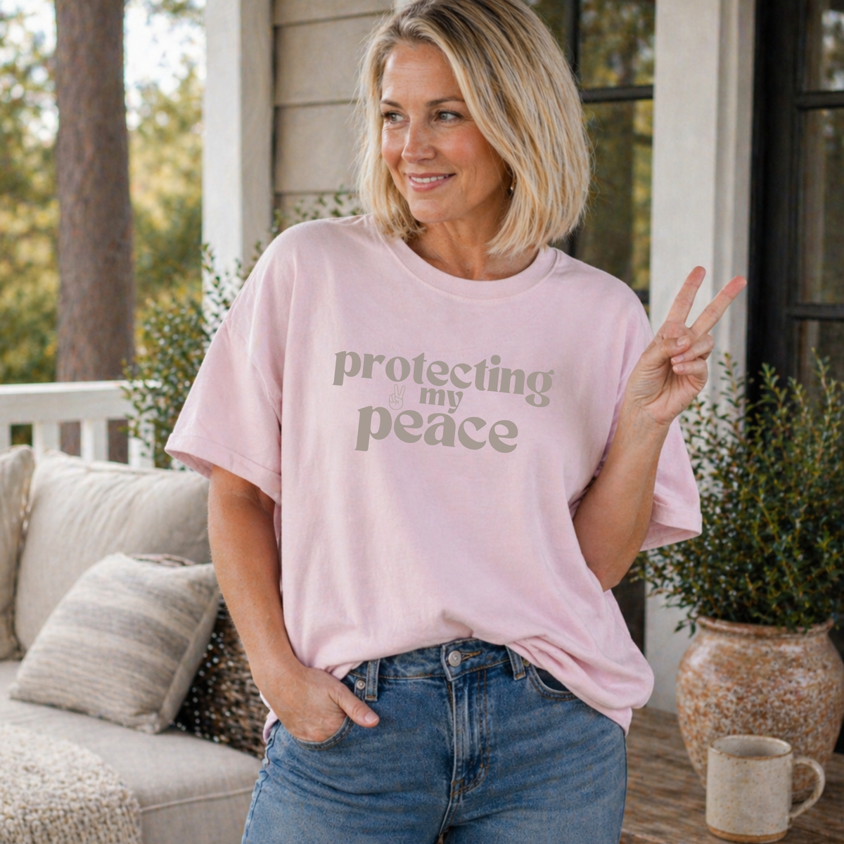 Woman wearing a pink t-shirt with 'protecting my peace' text, standing on a porch.