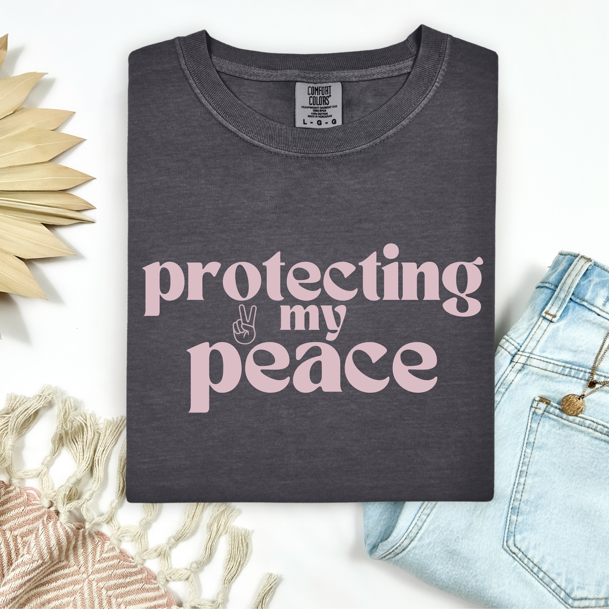 Dark gray t-shirt with 'protecting my peace' text in pink, displayed with denim jeans and decorative elements.