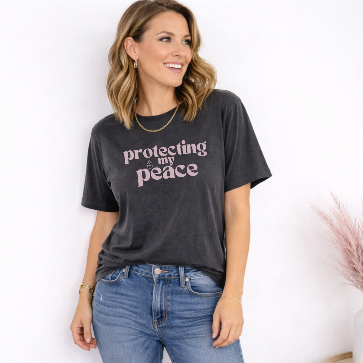 Woman wearing a black t-shirt with 'protecting my peace' text and blue jeans on a white background