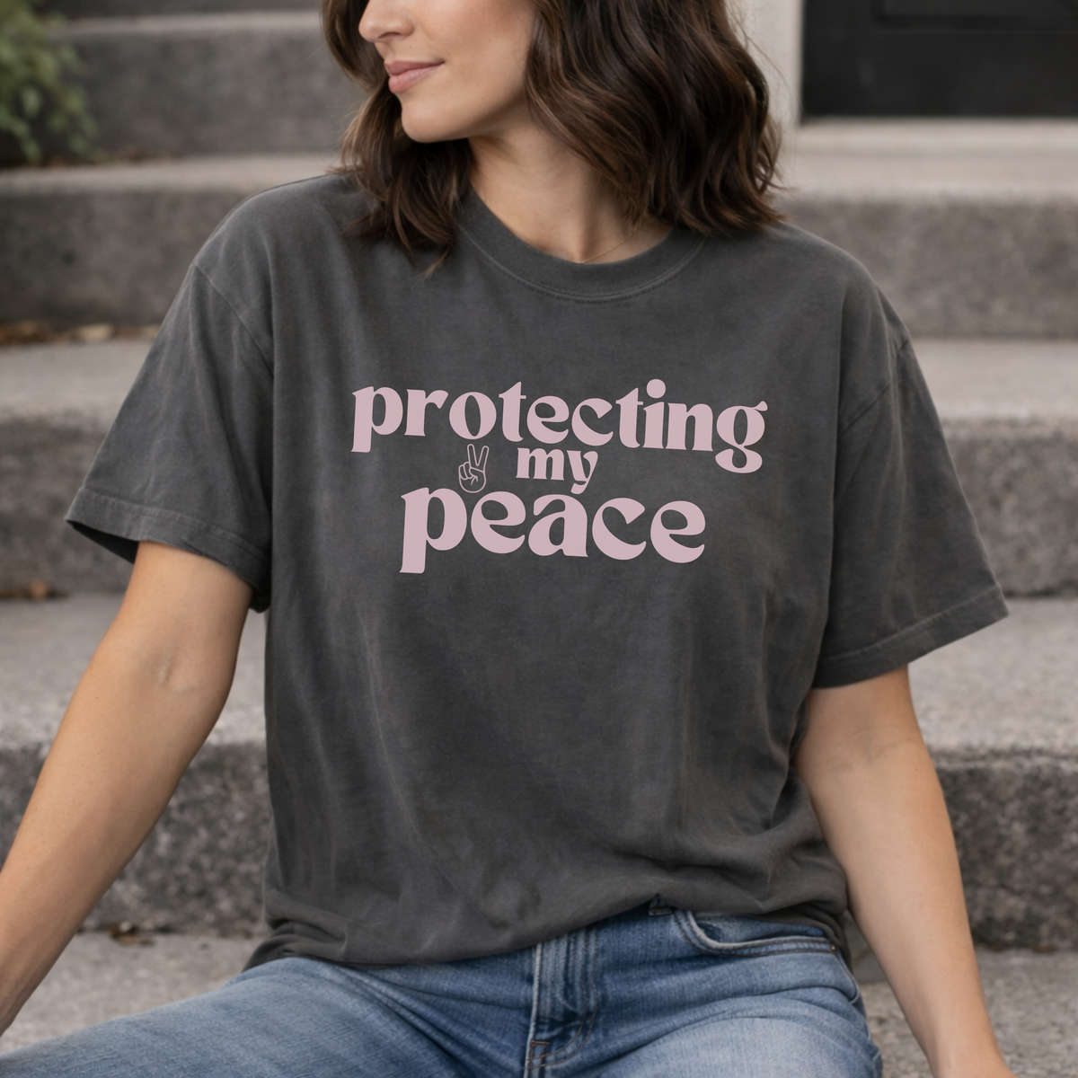 A woman wearing a vintage black t-shirt with 'protecting my peace' text sitting on steps.