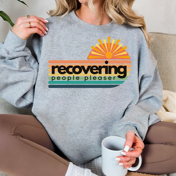 Person wearing a gray sweatshirt with a colorful graphic and text, holding a mug.