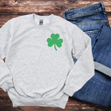 A light gray sweatshirt with a small pocket-sized shamrock on the top left of the sweatshirt.