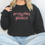 Person wearing a black sweatshirt with 'protecting my peace' text in pink.