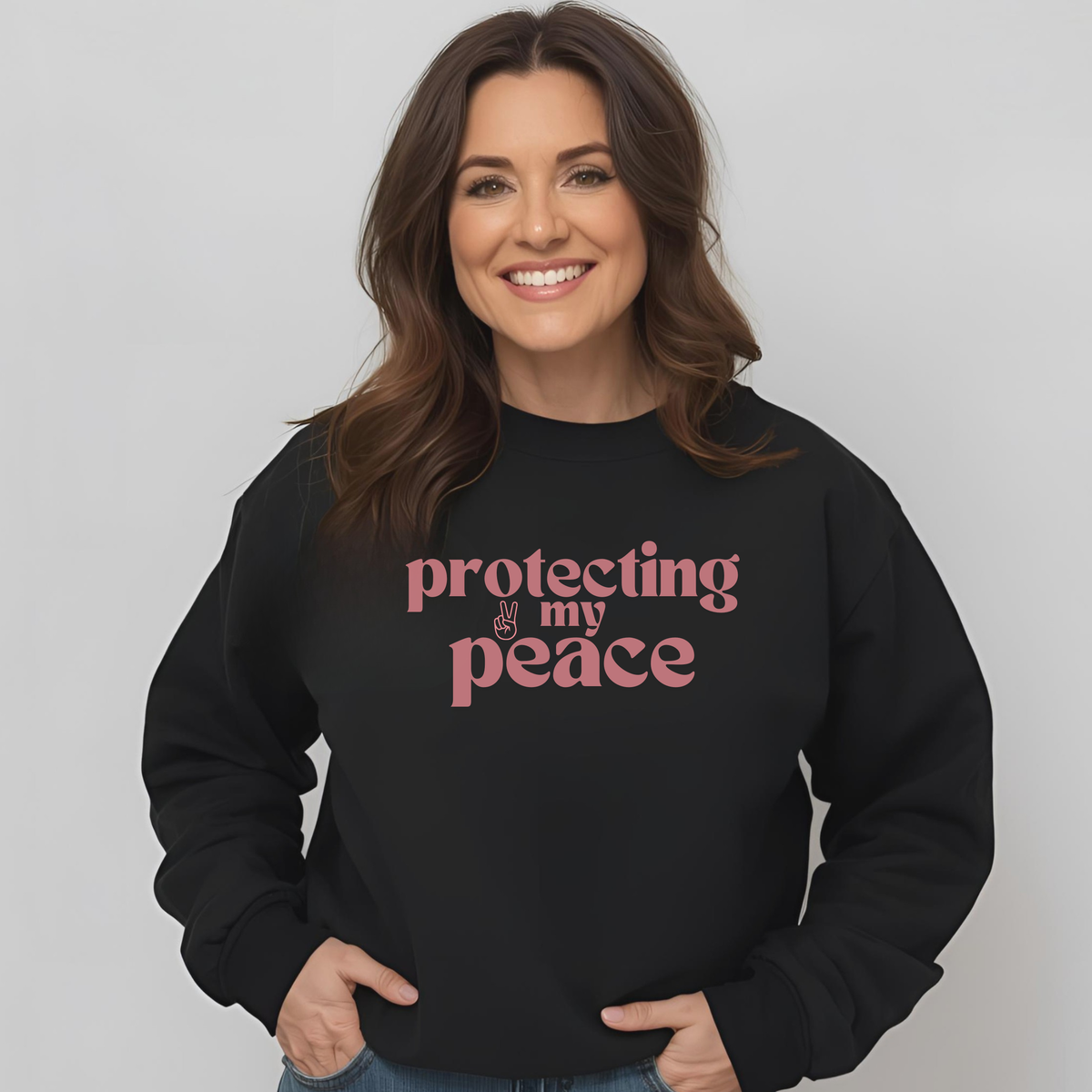 Woman wearing a black sweatshirt with 'protecting my peace' text on a plain background