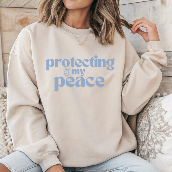 Person wearing a beige sweatshirt with 'protecting my peace' text in blue.