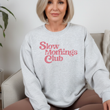 A woman wearing an ash gray sweatshirt with 'Slow Morning's Club' text in pink.