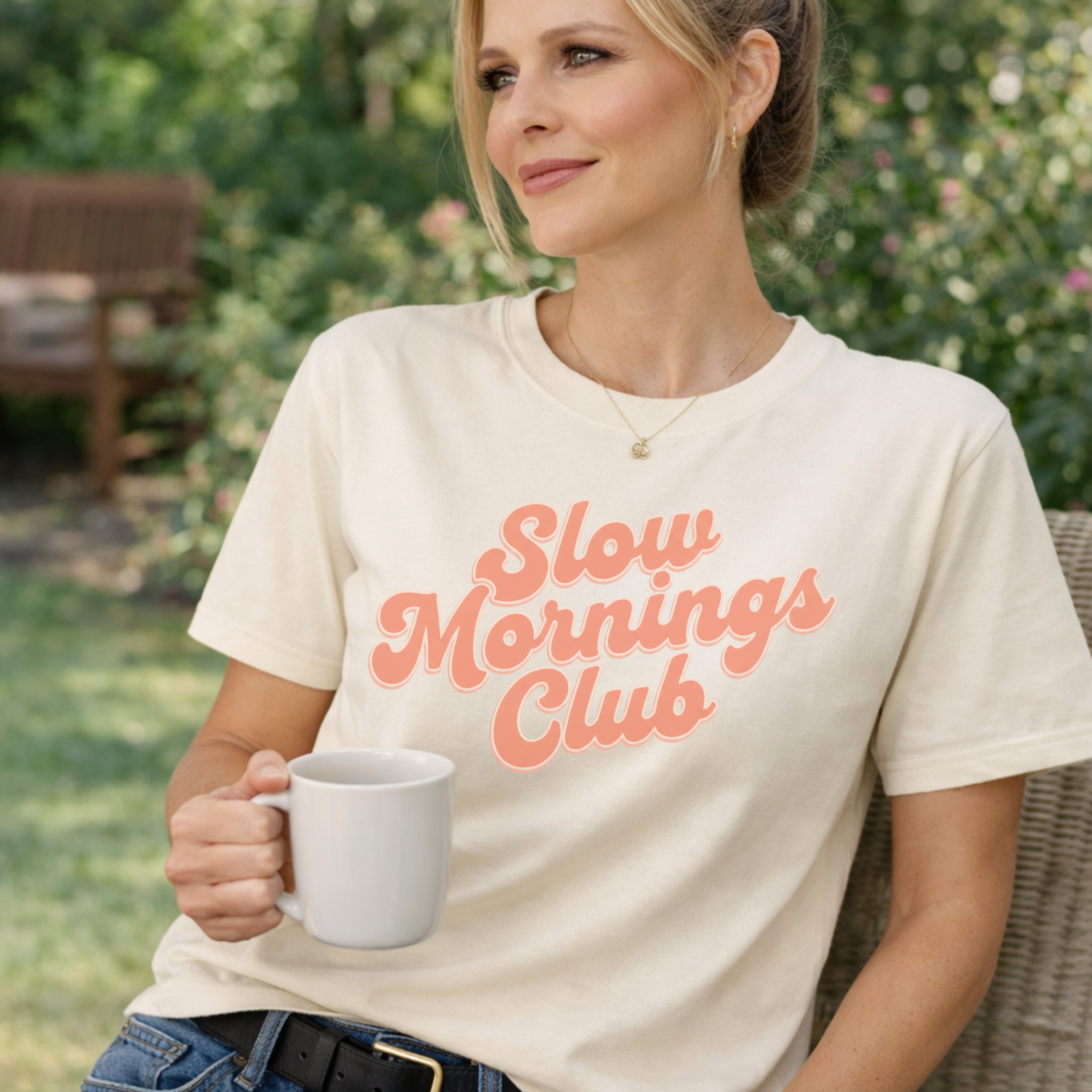 Woman wearing a 'Slow Mornings Club' t-shirt holding a mug outdoors.