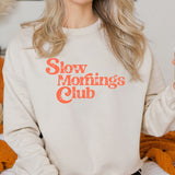 Woman wearing a beige sweatshirt with 'Slow mornings club' text in orange.