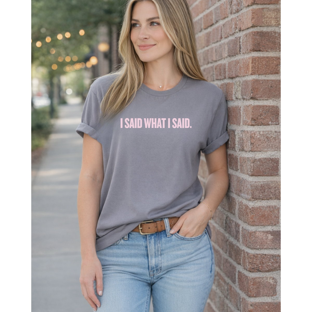 Woman wearing a gray t-shirt with 'I SAID WHAT I SAID' text, standing against a brick wall.
