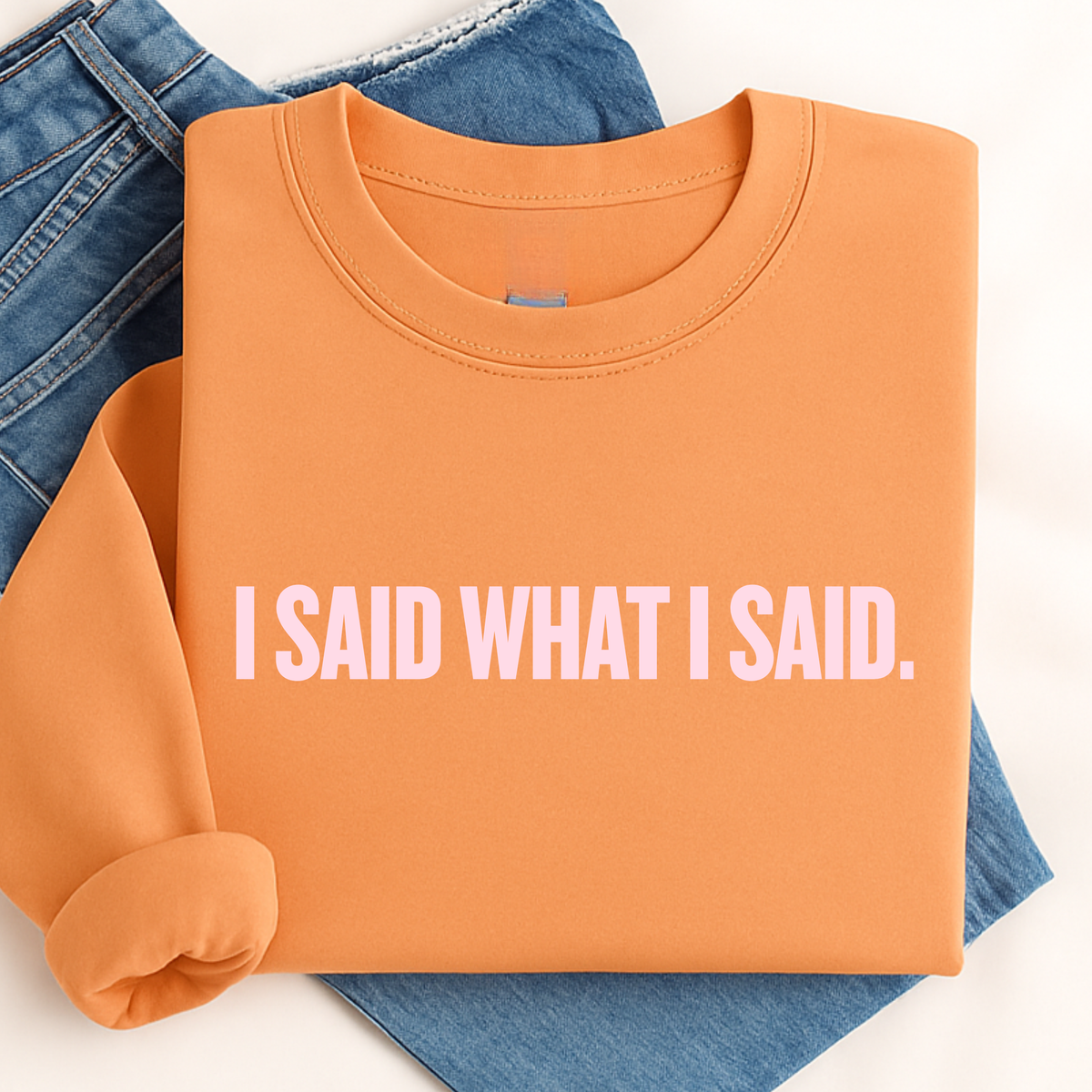 Folded tangerine orange sweatshirt with 'I SAID WHAT I SAID.' text on a white background