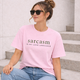 Woman wearing a pink t-shirt with 'sarcasm is my love language' text, sitting on steps.