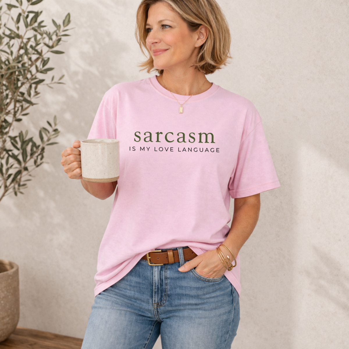 A womanwearing a pink t-shirt with 'sarcasm is my love language' text, holding a mug.