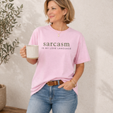 A womanwearing a pink t-shirt with 'sarcasm is my love language' text, holding a mug.