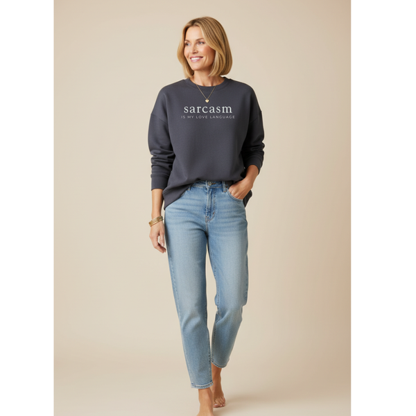 Woman wearing a dark gray sweater with 'sarcasm is my love language' text and light blue jeans on a beige background