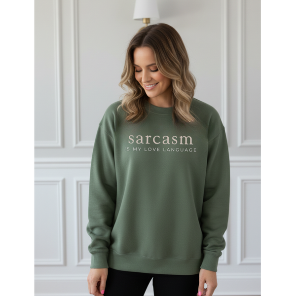 Woman wearing a green sweatshirt with 'sarcasm is my love language' text against a white paneled wall.