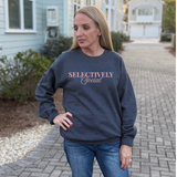 A Woman wearing a dark gray sweatshirt with 'SELECTIVELY Social' text in pink font, standing on a sidewalk.