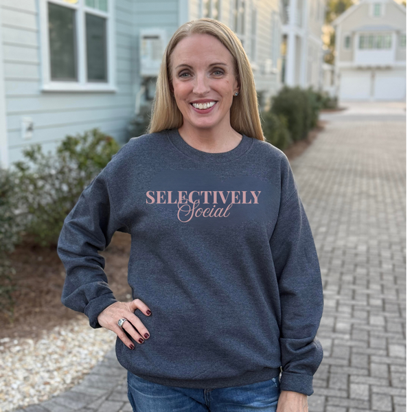 Woman wearing a dark heather gray sweatshirt with 'SELECTIVELY Social' text outdoors.