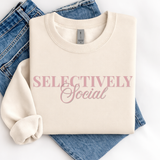 Folded cream sweatshirt with 'SELECTIVELY Social' text on blue jeans