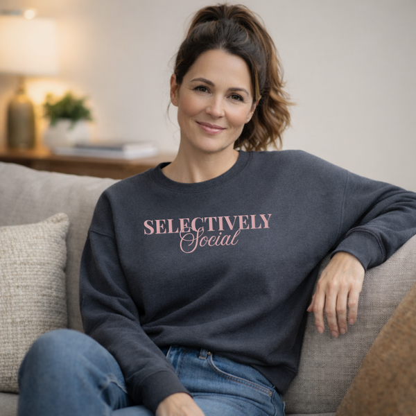 A Woman wearing a navy sweatshirt with 'SELECTIVELY Social' text in pink, sitting on a couch.
