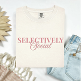 Ivory t-shirt with 'SELECTIVELY Social' text on a white background with denim jeans and decorative elements.