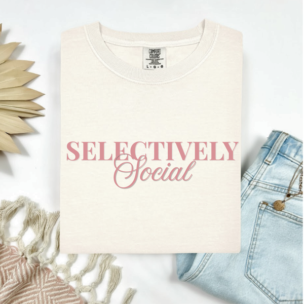 Ivory t-shirt with 'SELECTIVELY Social' text on a white background with denim jeans and decorative elements.