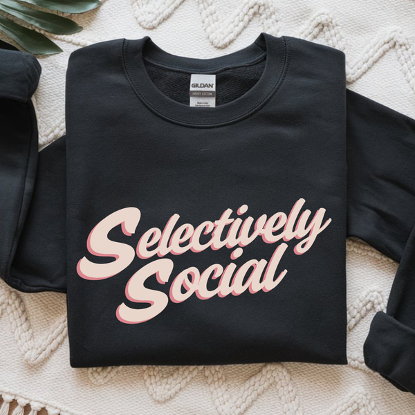 A folded black sweatshirt with the words "Selectively Social" written in a light pink script.