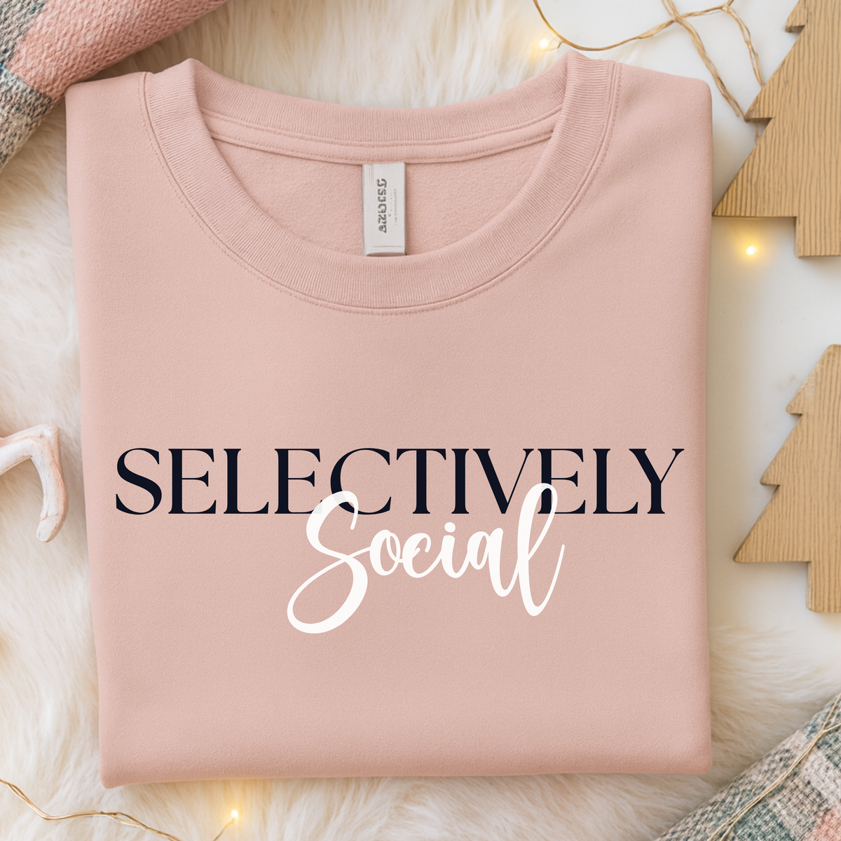 Folded blush pink sweatshirt with the words "Selectively Social" written across the front