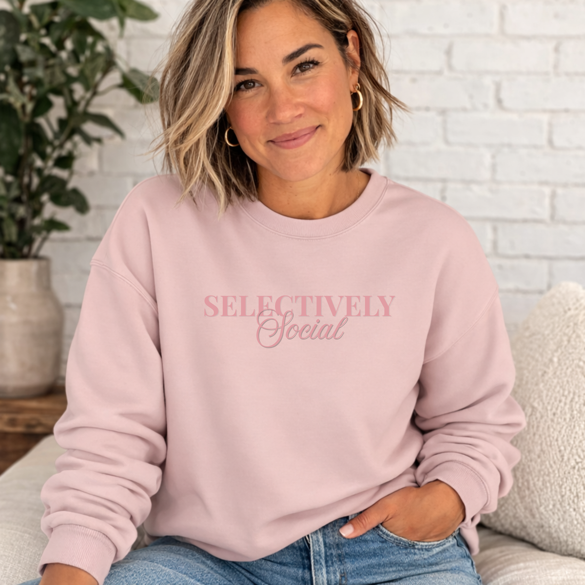 Woman wearing a pink sweatshirt with 'SELECTIVELY Social' text, sitting on a couch.