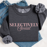 Dark gray folded sweatshirt with 'SELECTIVELY Social' text on a white background with jeans.