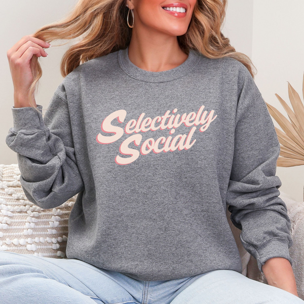 Woman sitting in a gray sweatshirt with the words "Selectively Social" written in a light pink script.