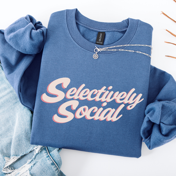 A folded blue sweatshirt with the words "Selectively Social" written in a light pink script.